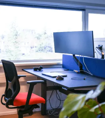 Werkplek bij Miller Digital met twee schermen en een rode bureaustoel bij het raam